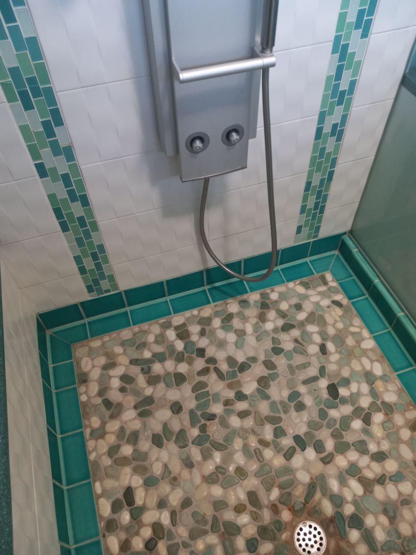 Small tiled shower stall with a wall-mounted control panel and drain in the floor.