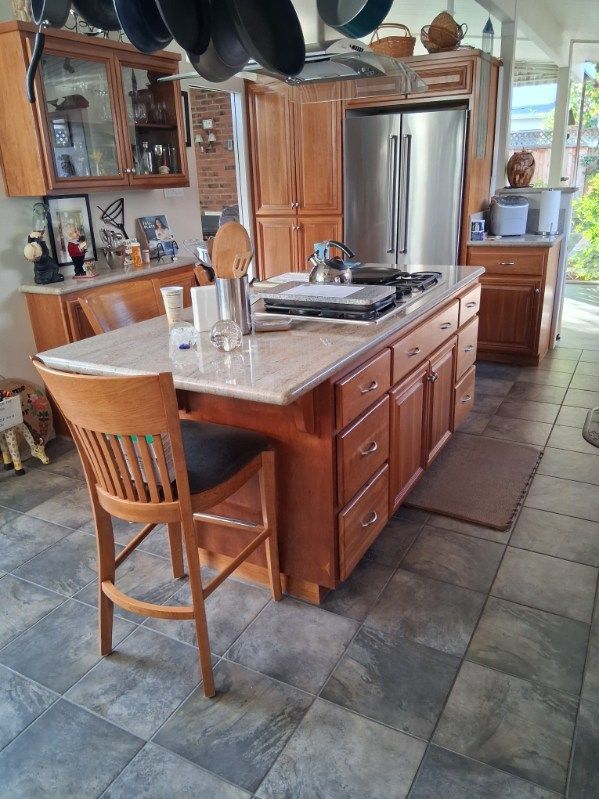Kitchen with wooden island, stainless steel refrigerator, and stone tile floor.