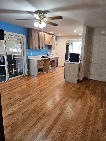 Empty kitchen with hardwood floors, blue backsplash, ceiling fan, and sliding glass door.
