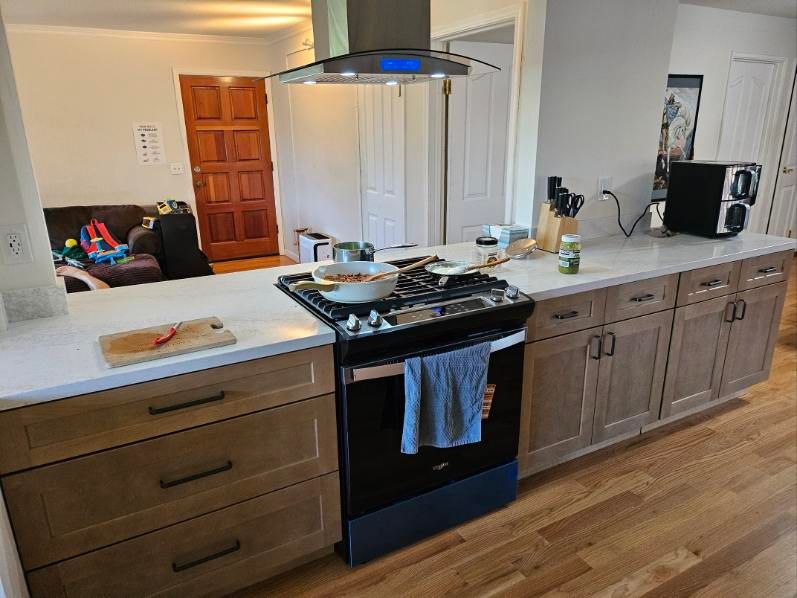 Modern kitchen with island, black stove, wood cabinets, and hardwood floor