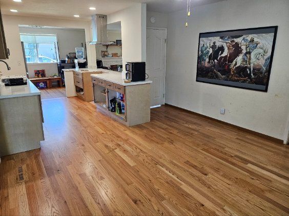 Empty open-plan living space with hardwood floors, kitchen island, and a large framed wall artwork.