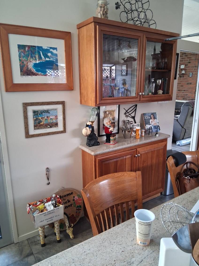 Dining room with wooden hutch, framed wall art, and a table with cups and a bottle.