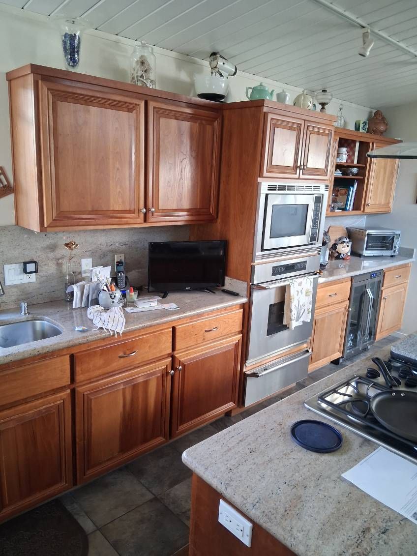 Wooden kitchen with stainless appliances, tan countertops, and a gas stove in the foreground.