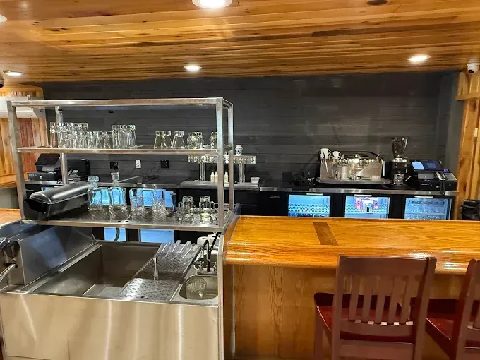 Bar interior with stainless steel sink, glass racks, and equipment behind a wooden bar.