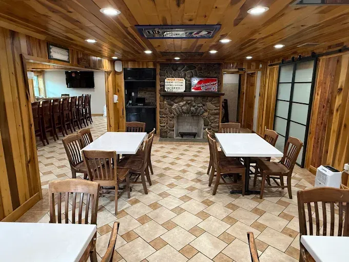 Restaurant interior with wooden paneling, tables, chairs, bar, and fireplace.