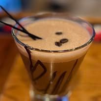 Close-up of a coffee cocktail in a glass with coffee bean garnish and a dark straw.