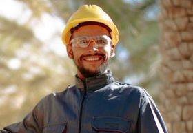 A man wearing a hard hat and safety glasses is smiling.