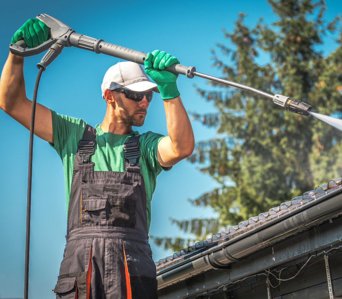 A man is cleaning the roof of a house with a high pressure washer.