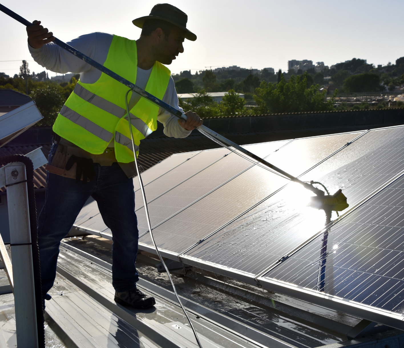 A man in a yellow vest is cleaning solar panels on a roof