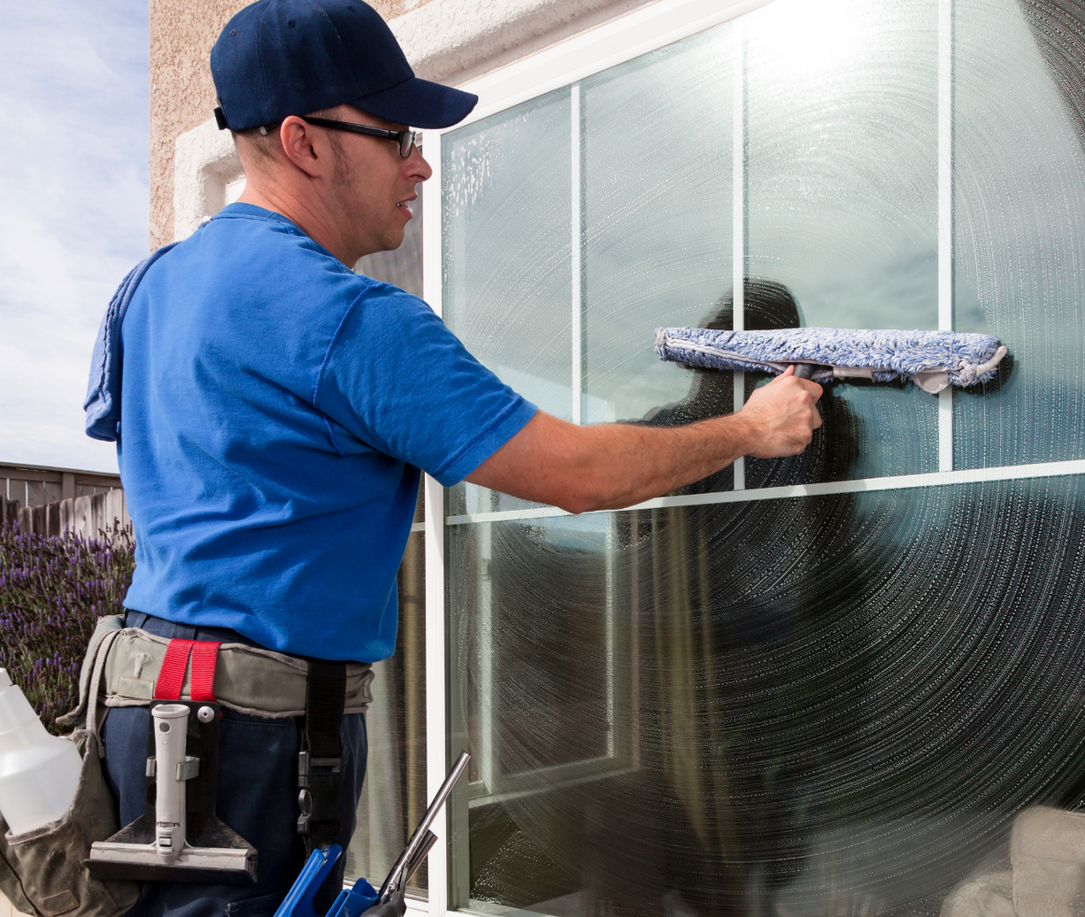 A man in a blue shirt is cleaning a window with a squeegee.