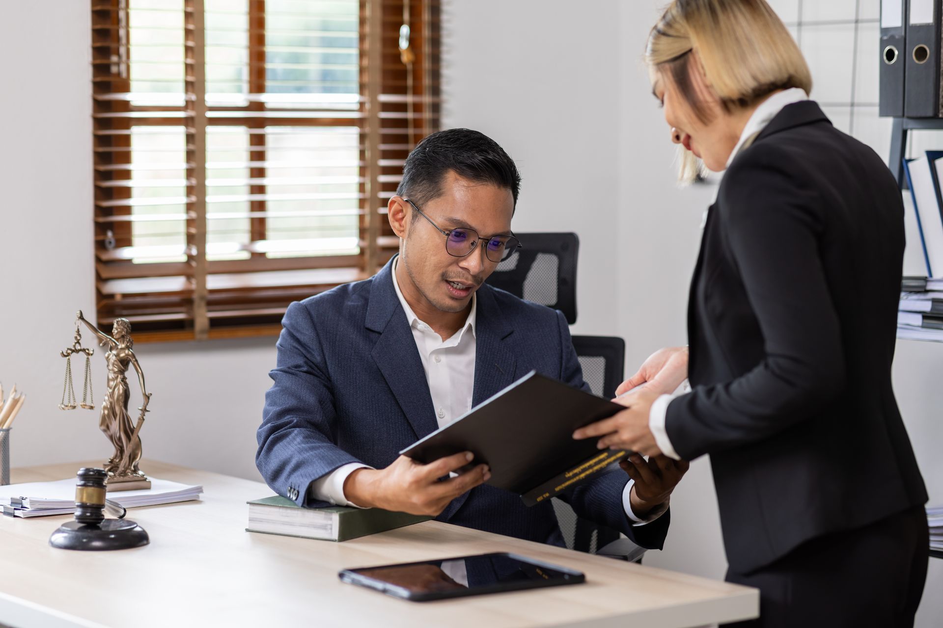 A professional in a suit reviews a folder while interacting with a colleague in a law office setting.