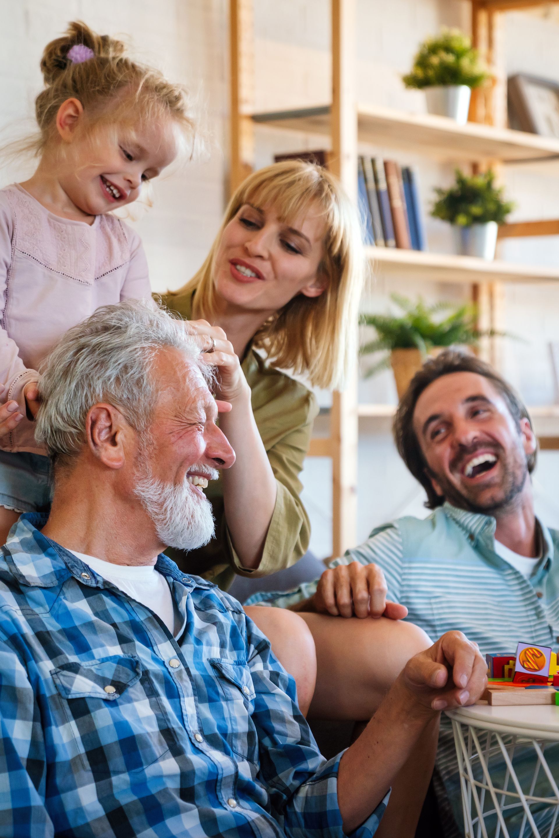 A group of people laughing together in a brightly lit room with a wooden bookshelf in the background.