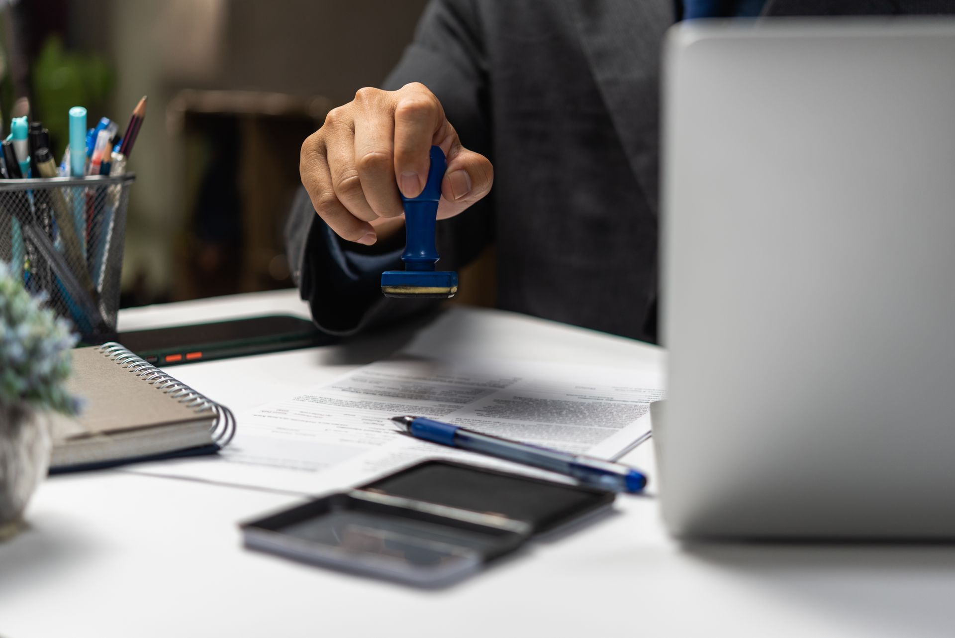 A professional hand stamping a document on a desk with a laptop, stationery, and ink pad nearby.