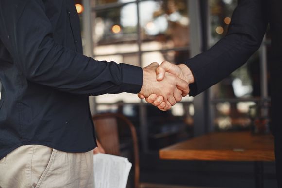 Two people in dark shirts shaking hands in a professional setting.