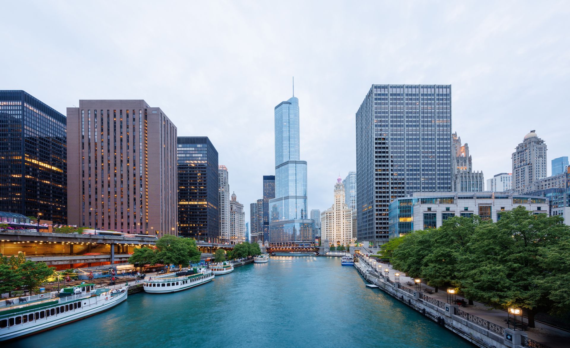 A view of the Chicago River flowing between tall downtown skyscrapers and boats moored along the banks.