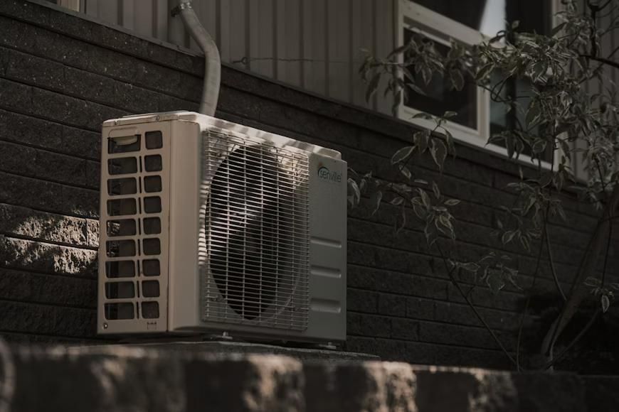 Black-and-white picture of an HVAC system on a wall next to a tree