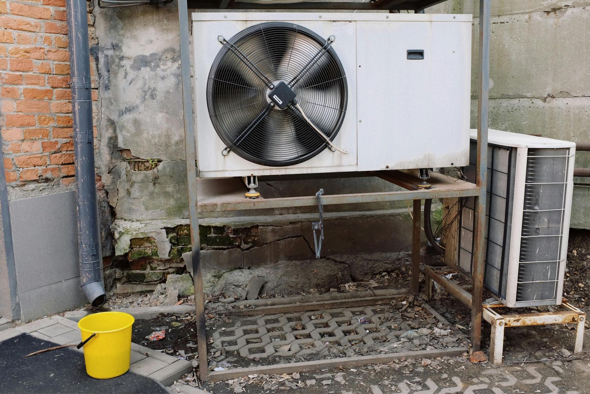 External air conditioner unit placed on metal platform near a building wall.