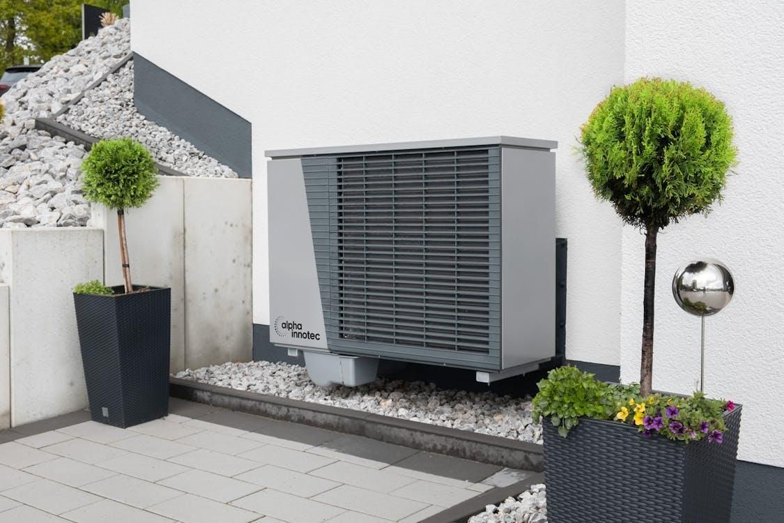 A modern HVAC unit placed against a wall with potted plants in the surroundings.