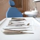 Dental instruments laid out on a tray in a dentist's office, with a blue chair in the background.