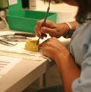 Person uses a tool to work on a yellow dental mold, with other tools and a green container nearby.