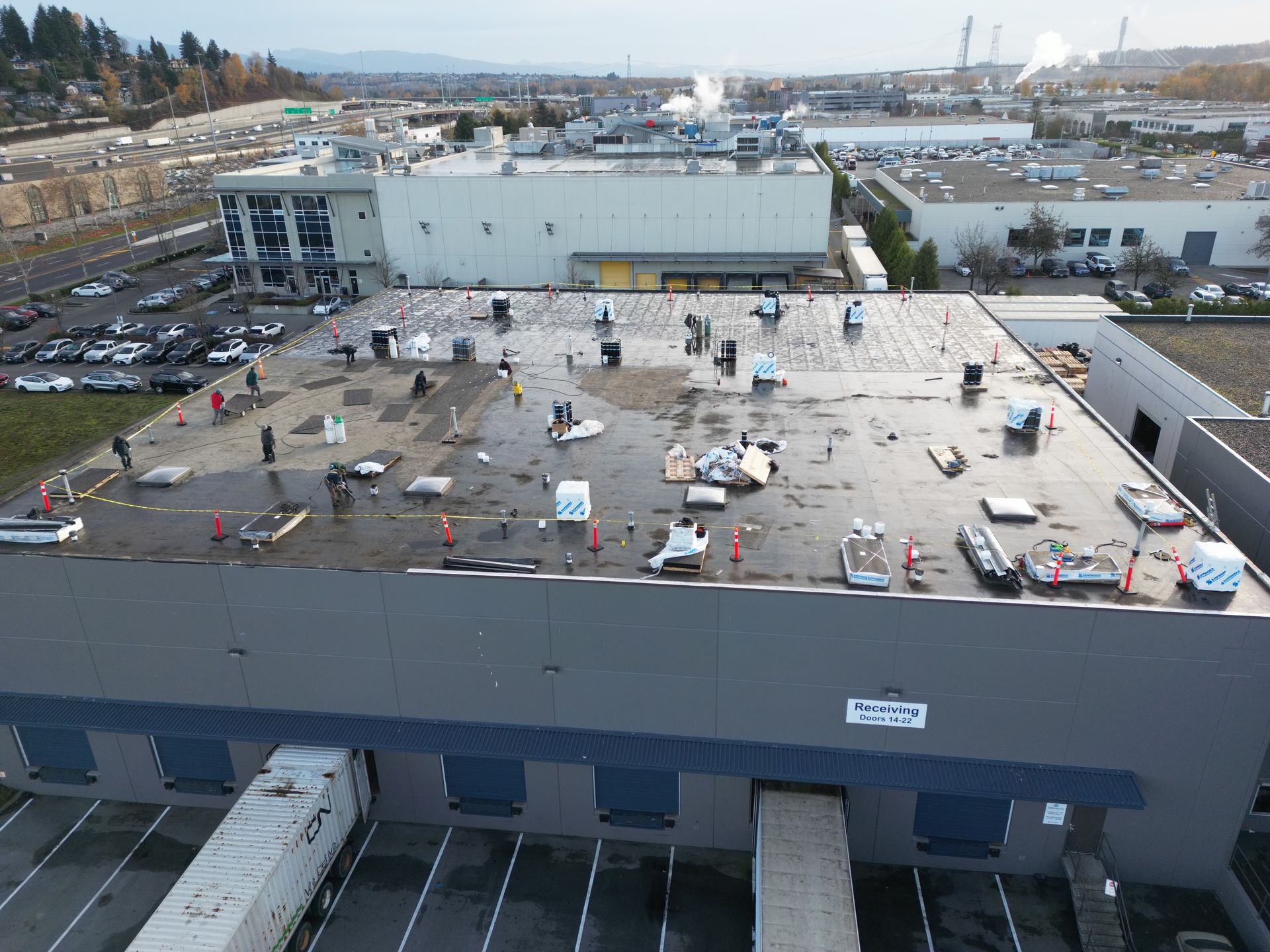 Warehouse roof with debris, trucks at loading docks, industrial buildings in the background.