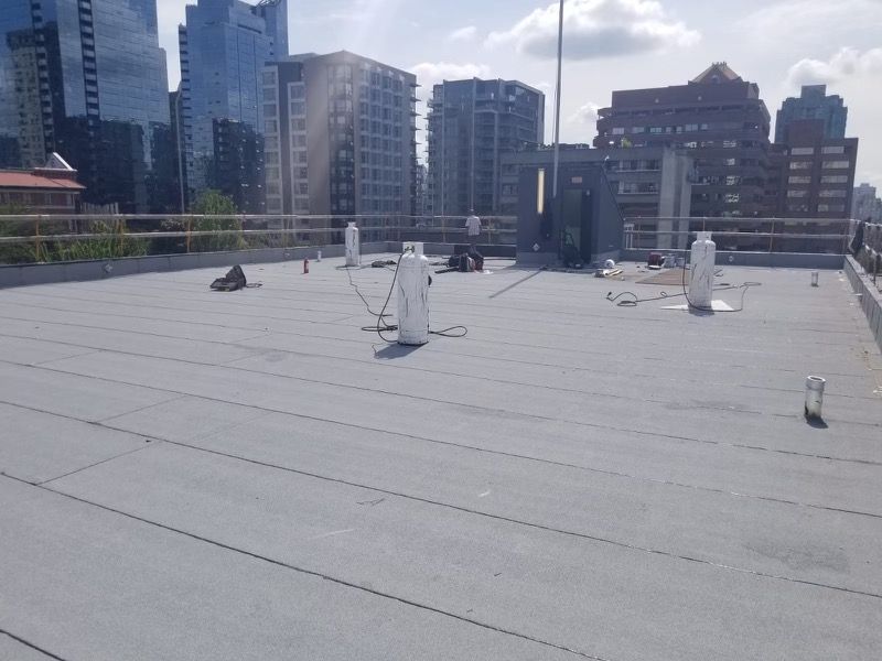 Rooftop with gray surface, several white tanks, and city buildings in the background on a sunny day.