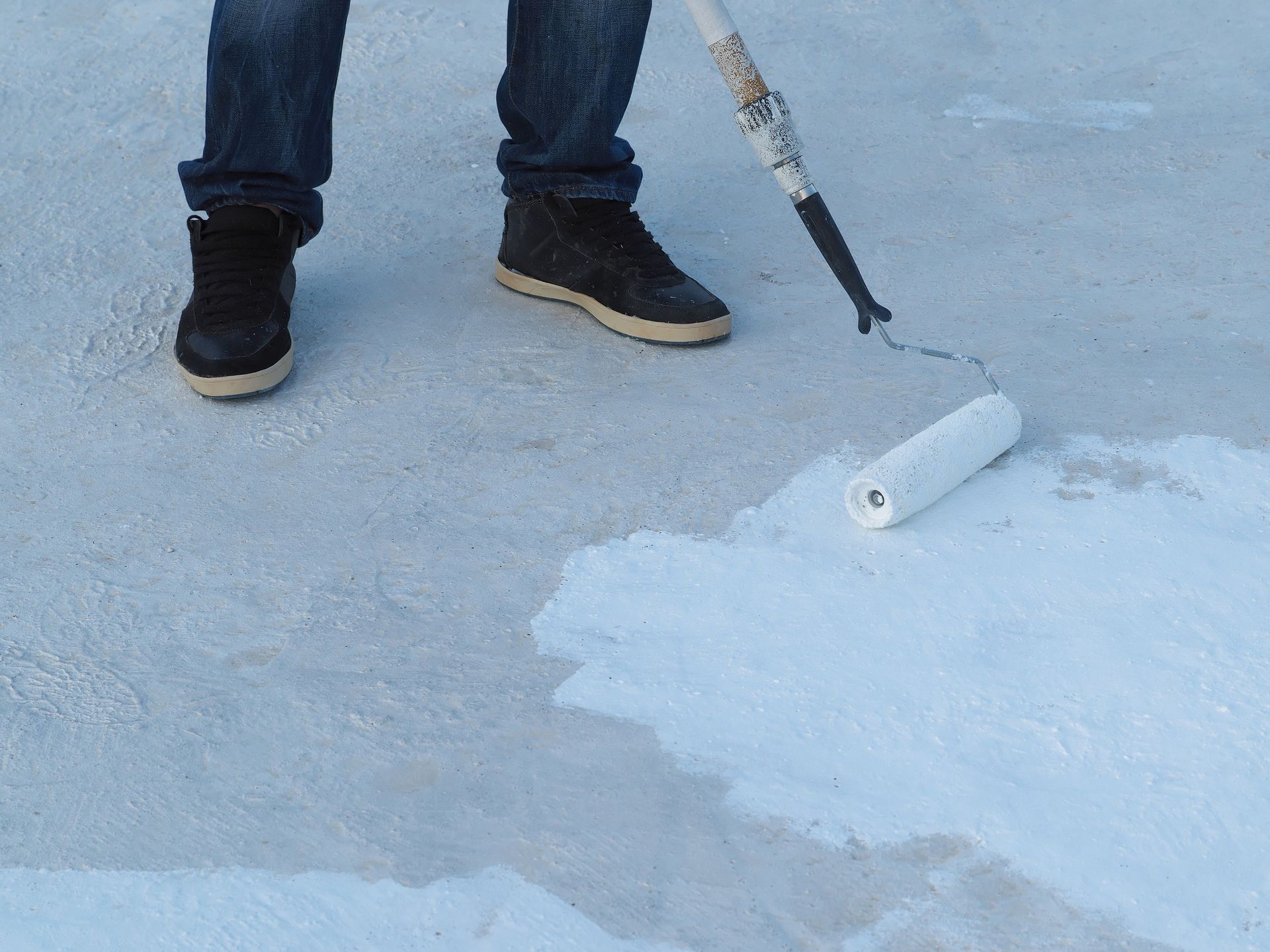 A person is painting a concrete surface with a roller.