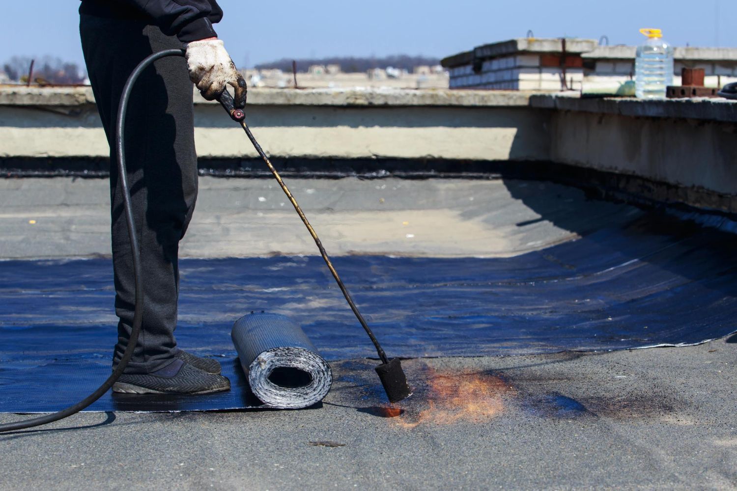 Roofer using a torch to seal roofing material on a flat roof.