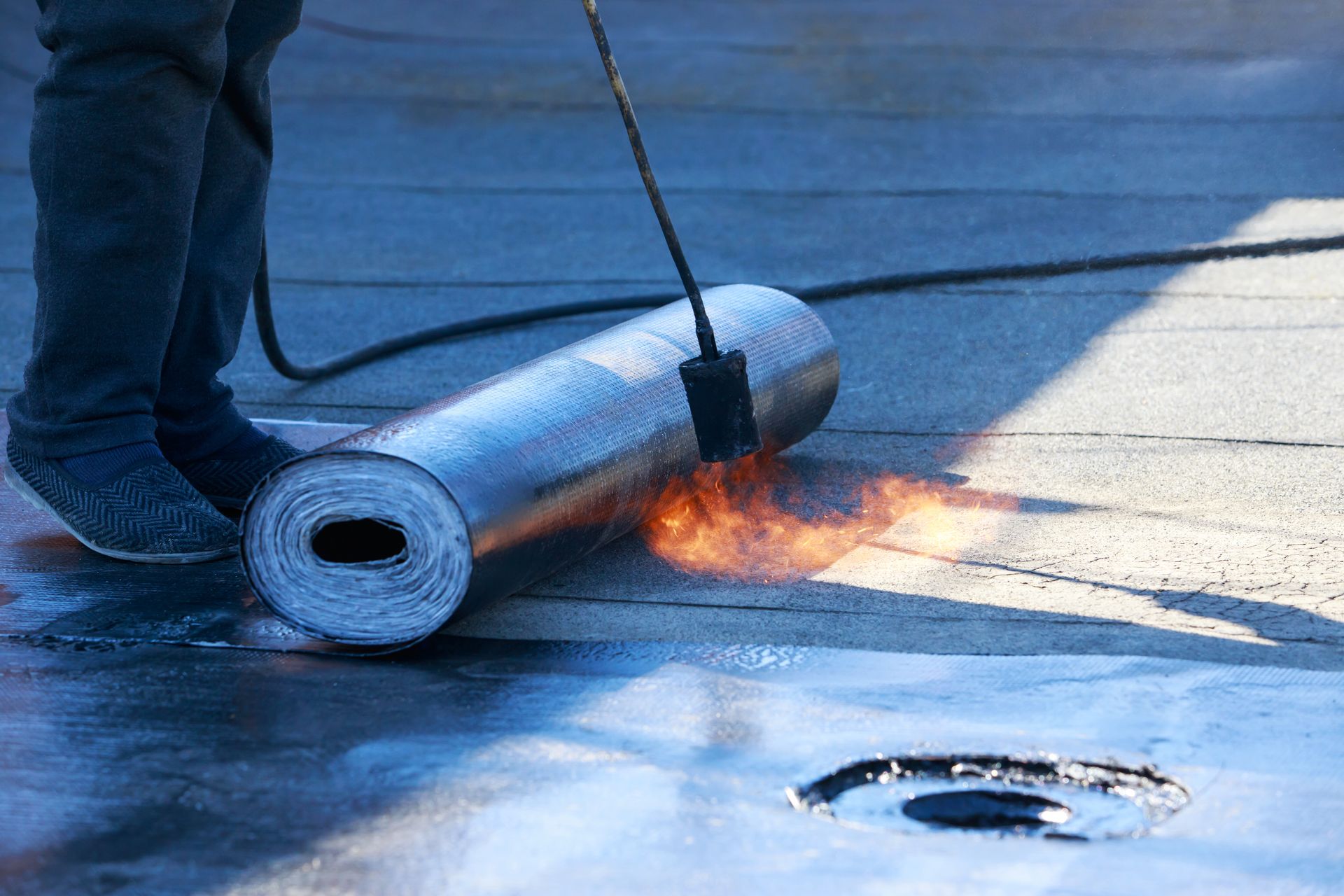 Roofer using a torch to adhere rolled roofing material to a flat roof.