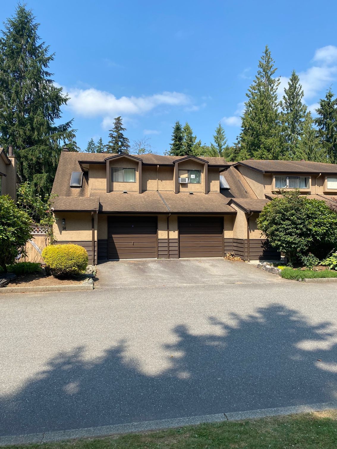 A house with two garages is surrounded by trees on a sunny day