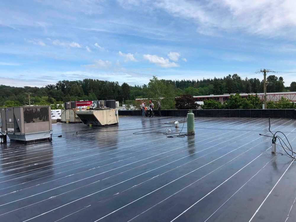 Rooftop with dark panels, equipment, and workers under a cloudy sky.