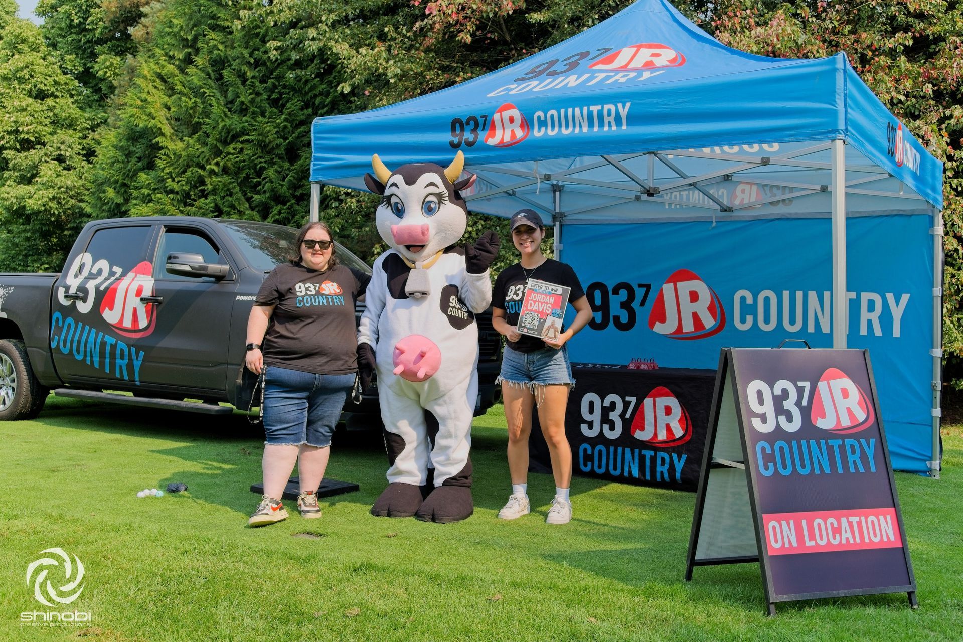 A cow mascot is standing next to two women and a truck.