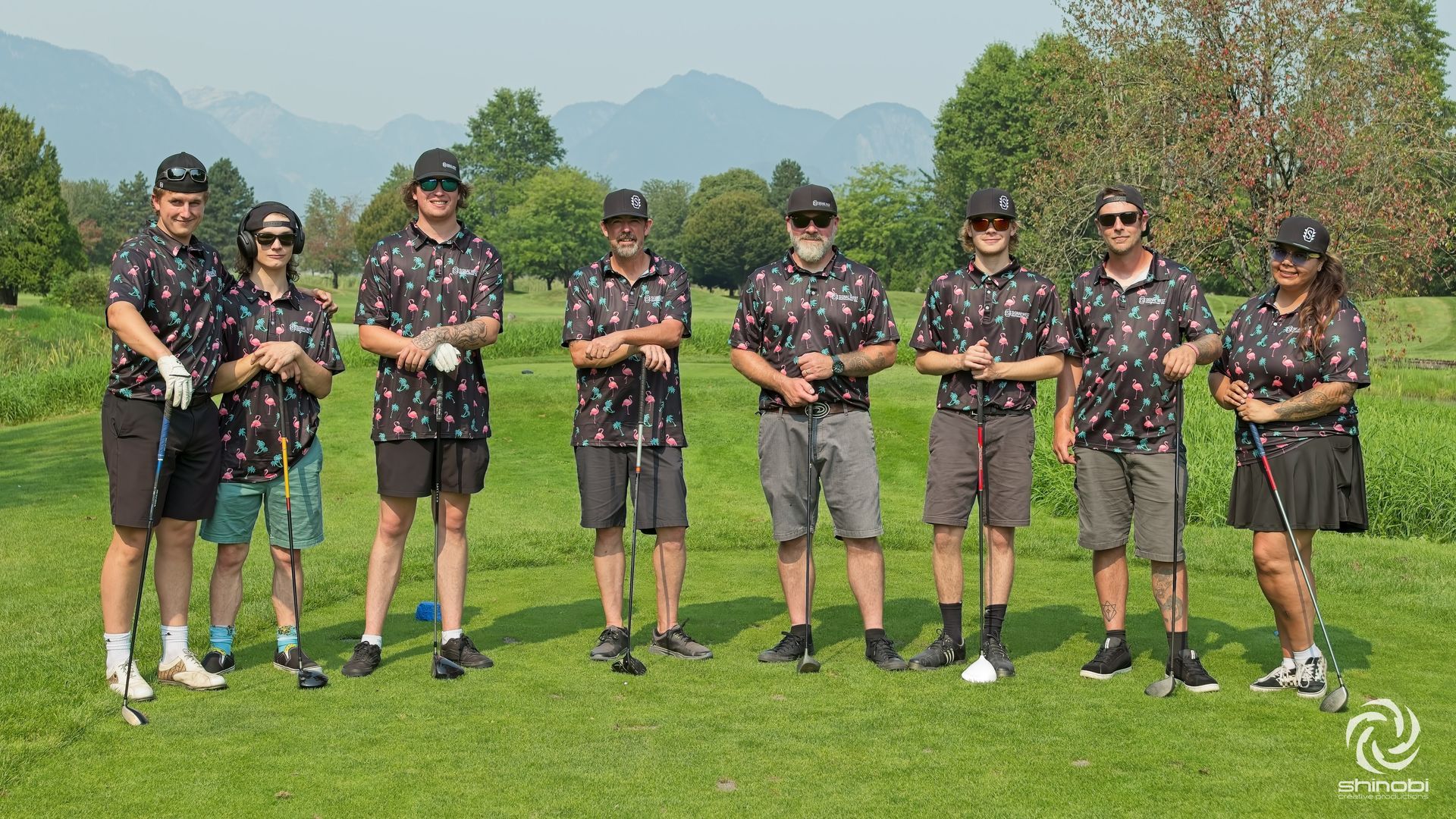 A group of people are standing in a row on a golf course holding golf clubs.
