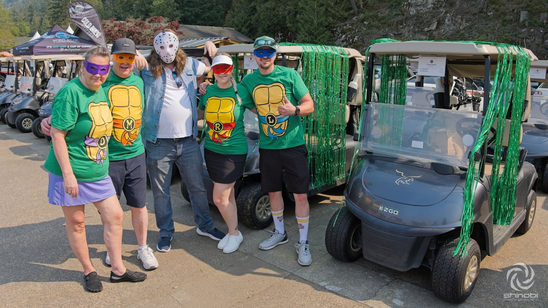 A group of people wearing green turtle shirts are posing for a picture in front of golf carts.