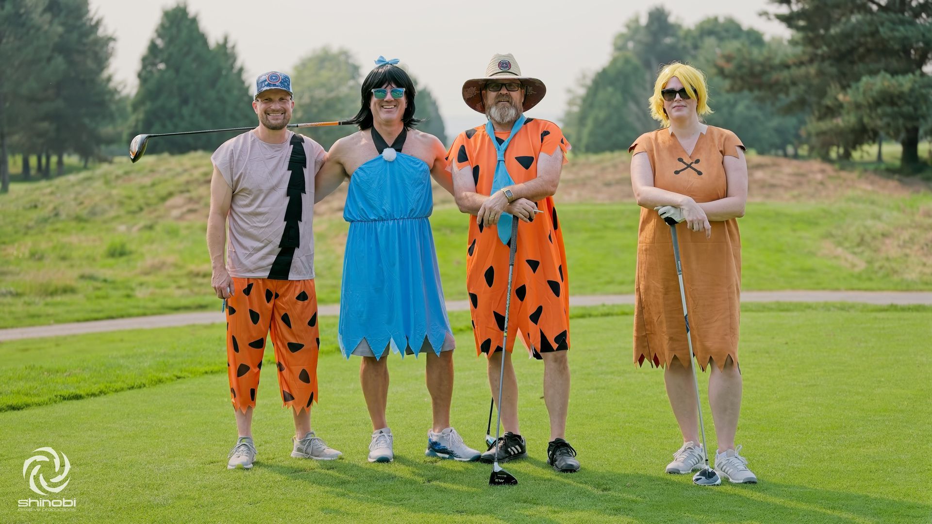 A group of people dressed as the flintstones are standing on a golf course holding golf clubs.