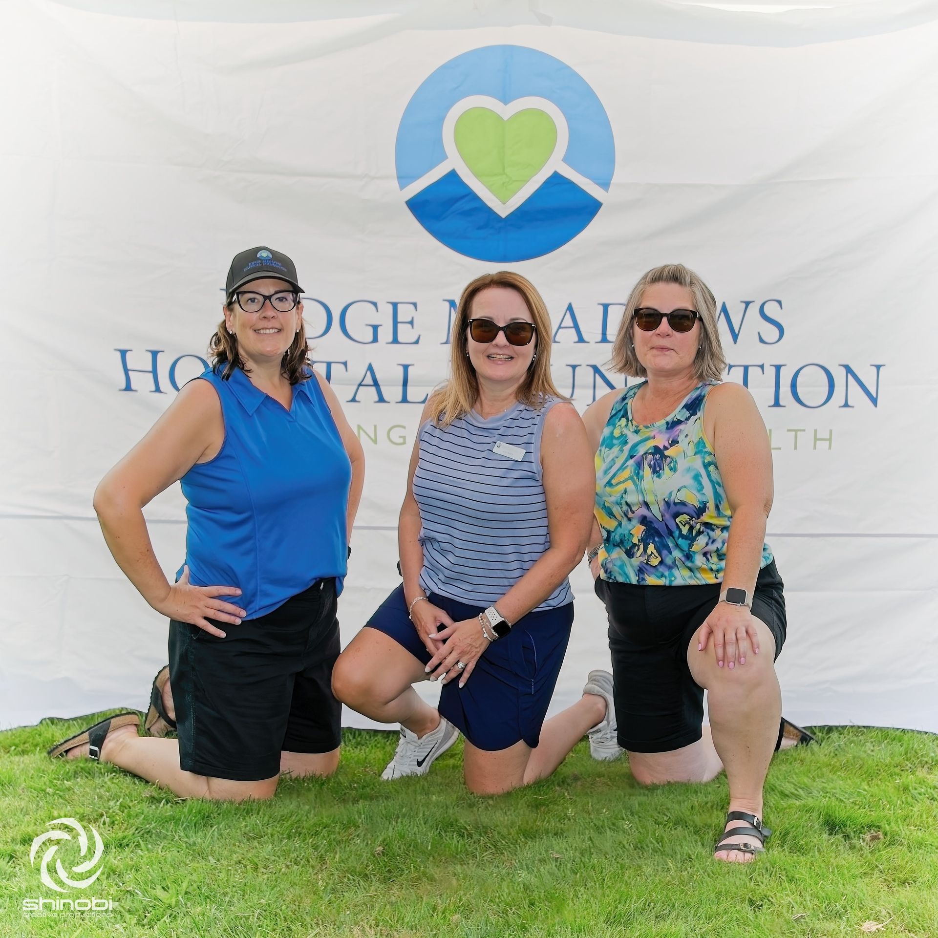 Three women are posing for a picture in front of a hospital foundation banner