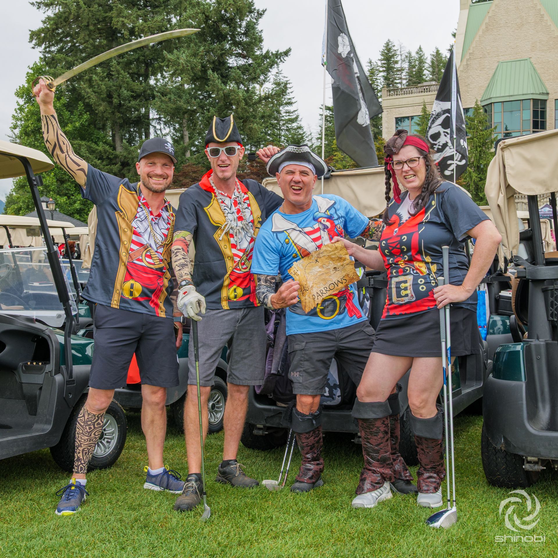 Four people in pirate costumes posing on a golf course. One raises a sword, another holds a treasure map.