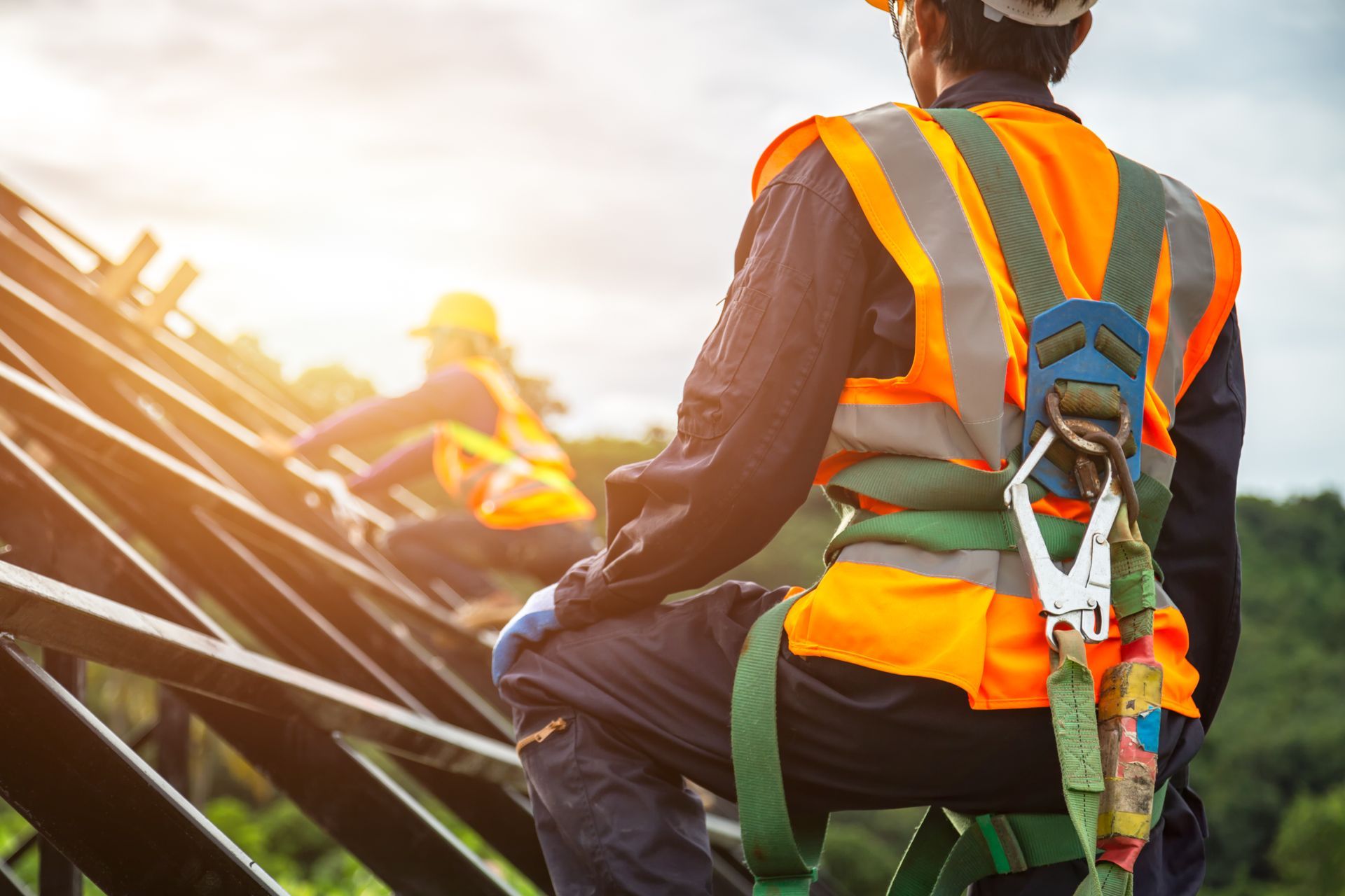 A construction worker wearing a safety harness is sitting on a metal structure.