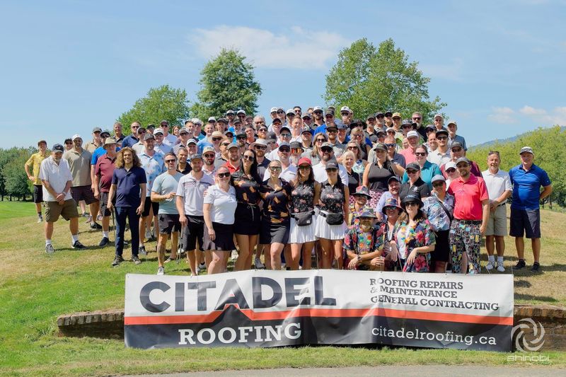 A large group of people are standing in front of a sign that says citadel roofing.