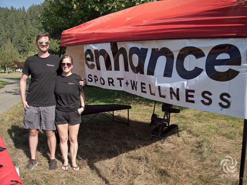 A man and a woman are standing in front of a sign that says enhance sport wellness.