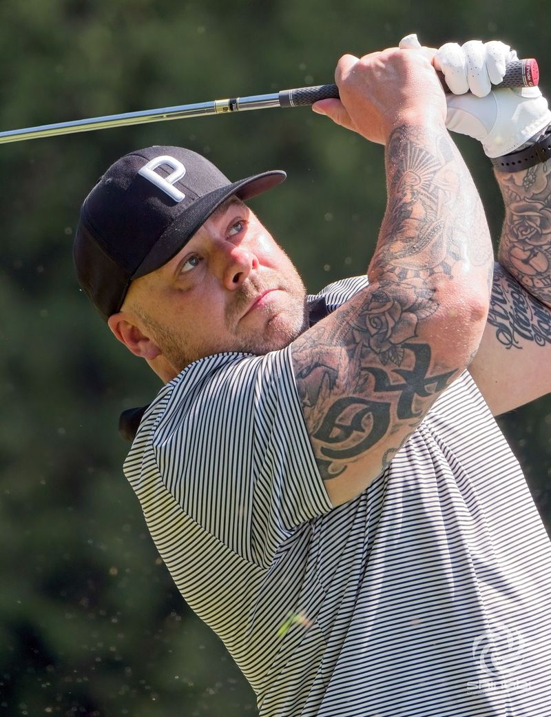 A man with tattoos is swinging a golf club on a golf course.