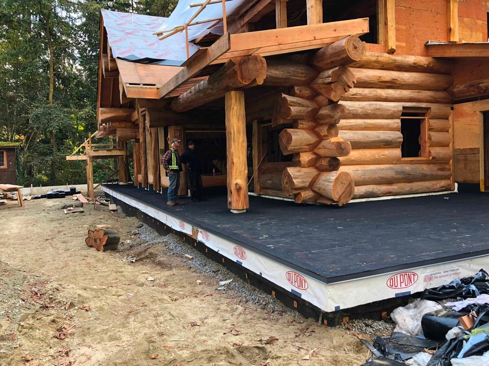 A man is standing in front of a log cabin under construction.