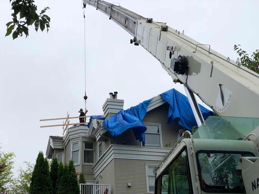 A large white crane is working on a house with a blue tarp on the roof