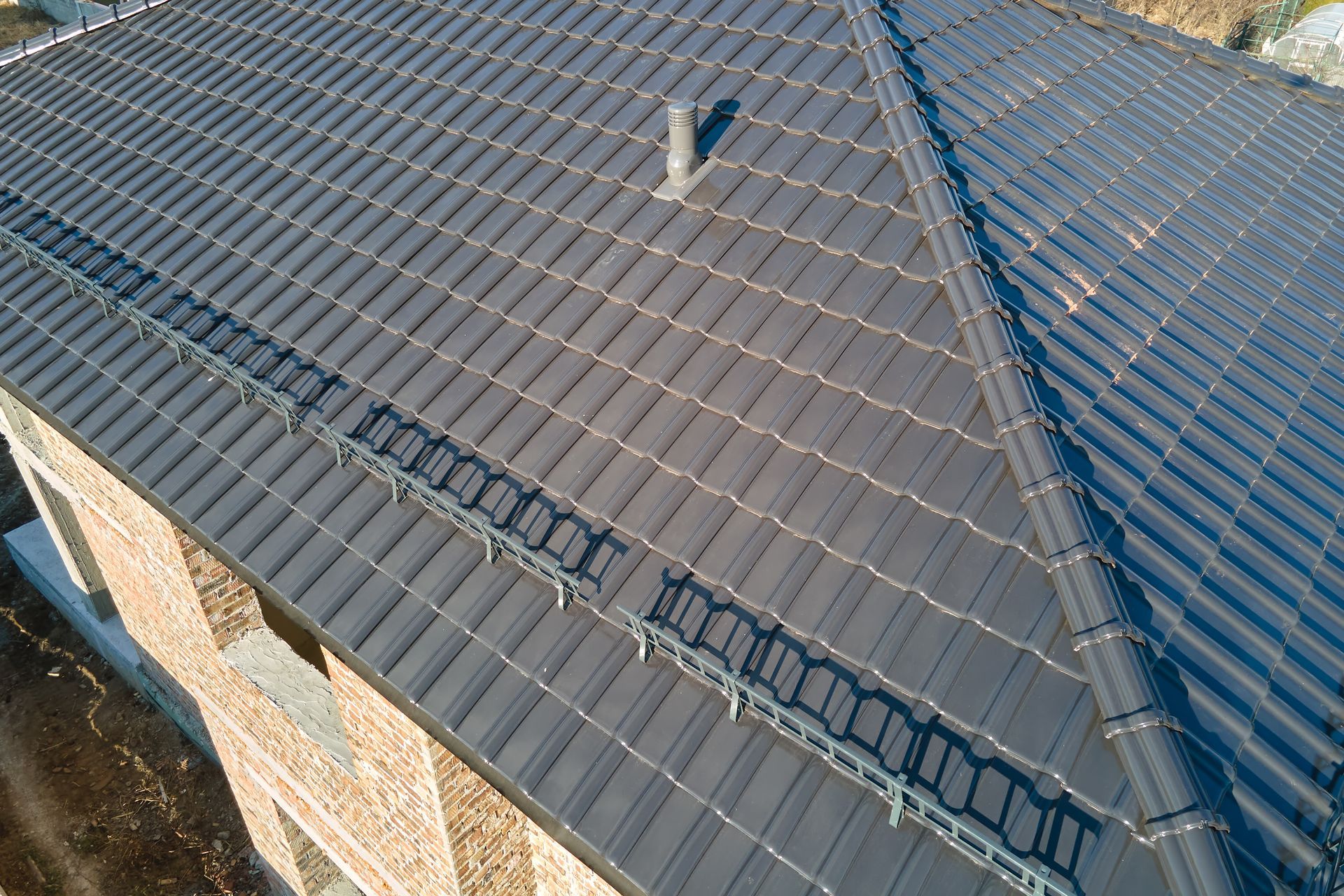 Dark gray tile roof with a chimney and a metal gutter system on a brick building.