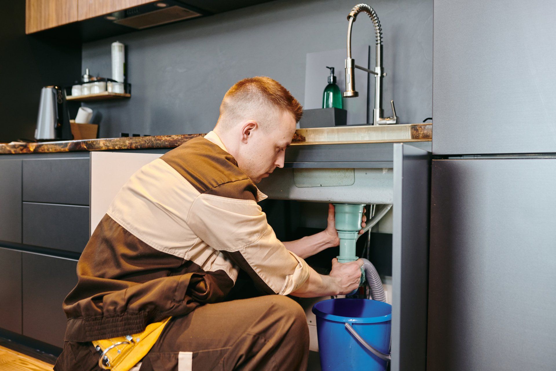 A man is fixing a sink in a kitchen.