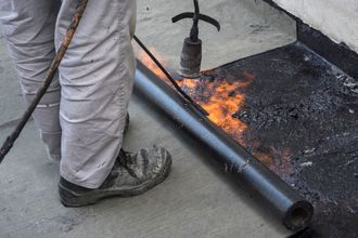 A person is using a torch to heat a roll of asphalt.