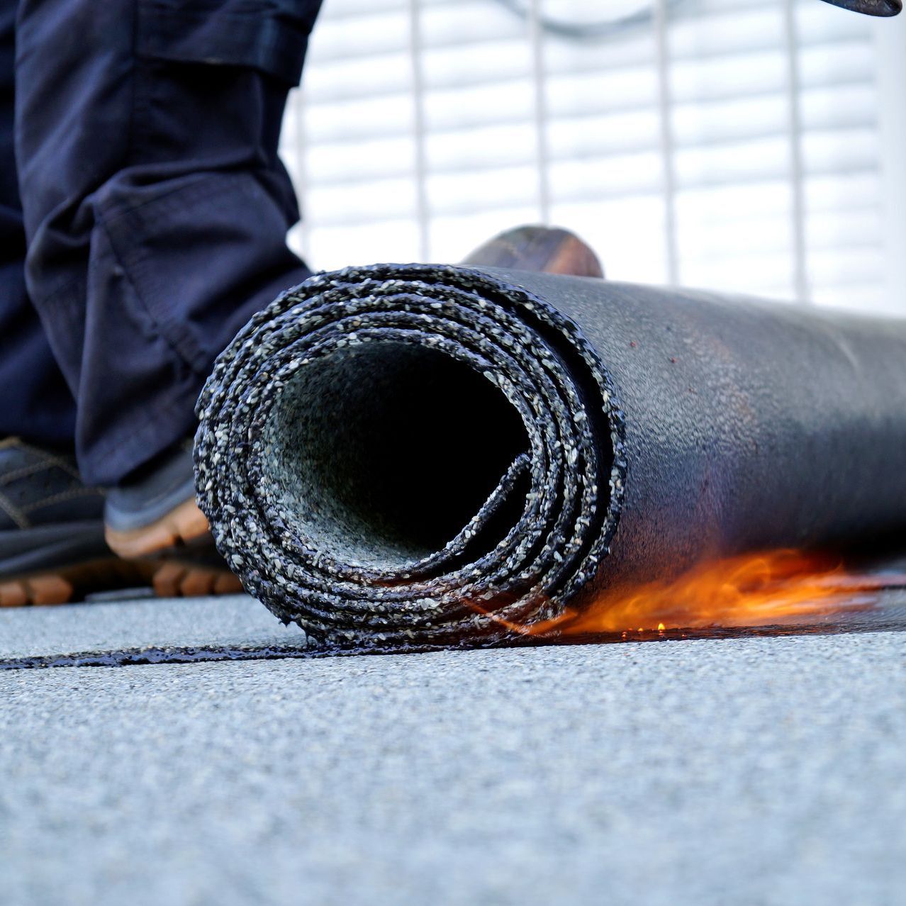 A person is rolling a roll of asphalt on the ground