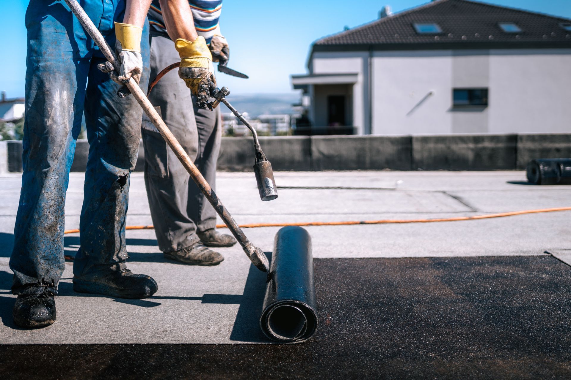 Two men are working on a roof with a torch.