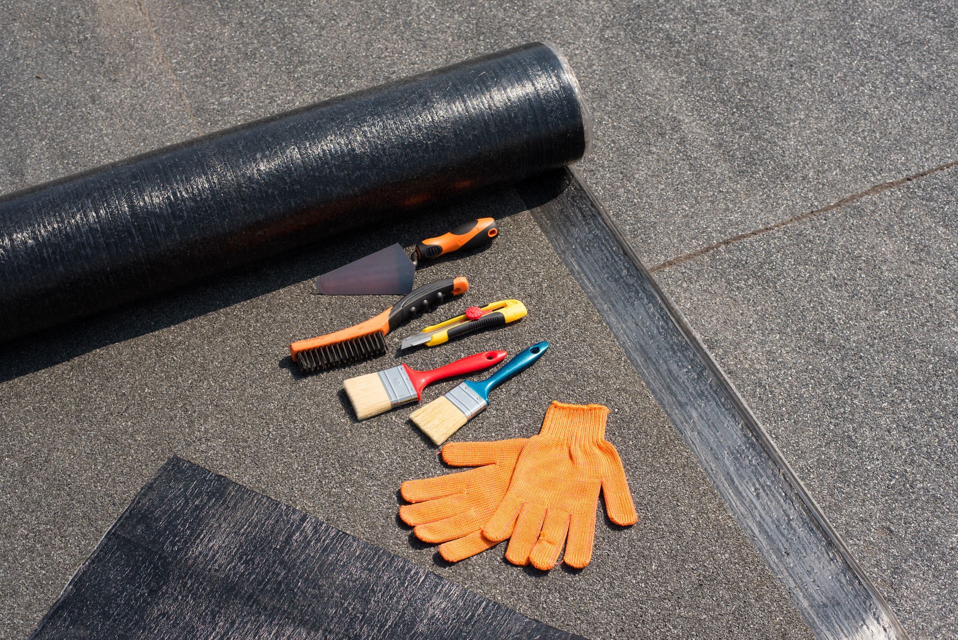 A roll of roofing material , tools , and gloves on the ground.