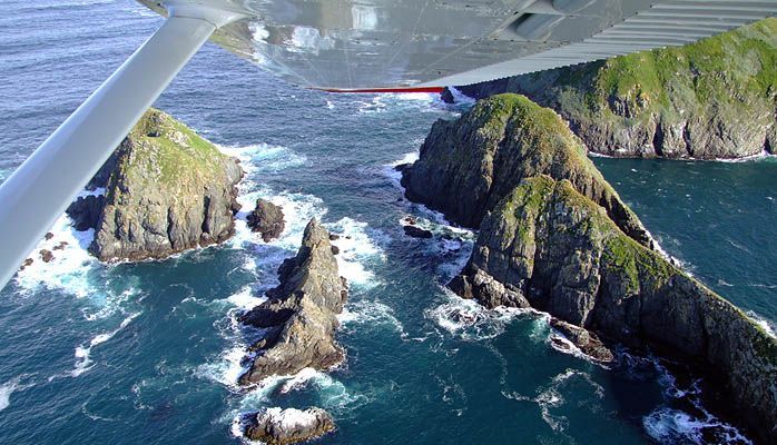 A plane is flying over a cliff overlooking the ocean